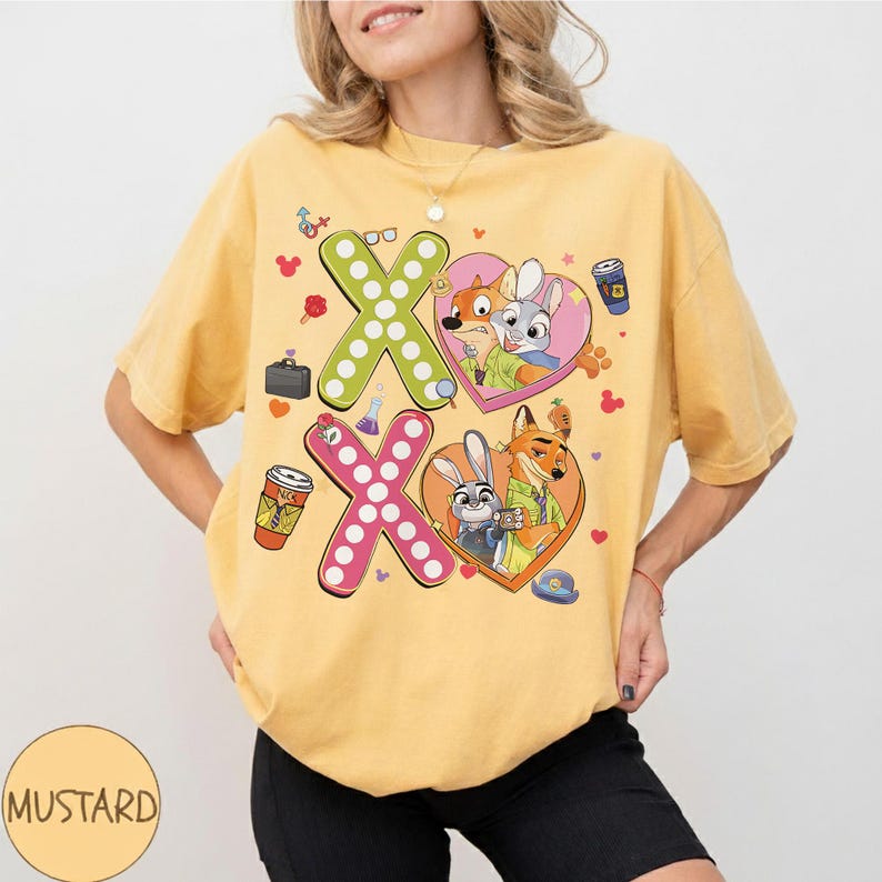 May include: Mustard-colored t-shirt featuring a graphic design with the text "XO" and cartoon characters in heart-shaped frames. The design includes images of a fox, a rabbit, and other themed elements. The shirt is a casual, unisex style.