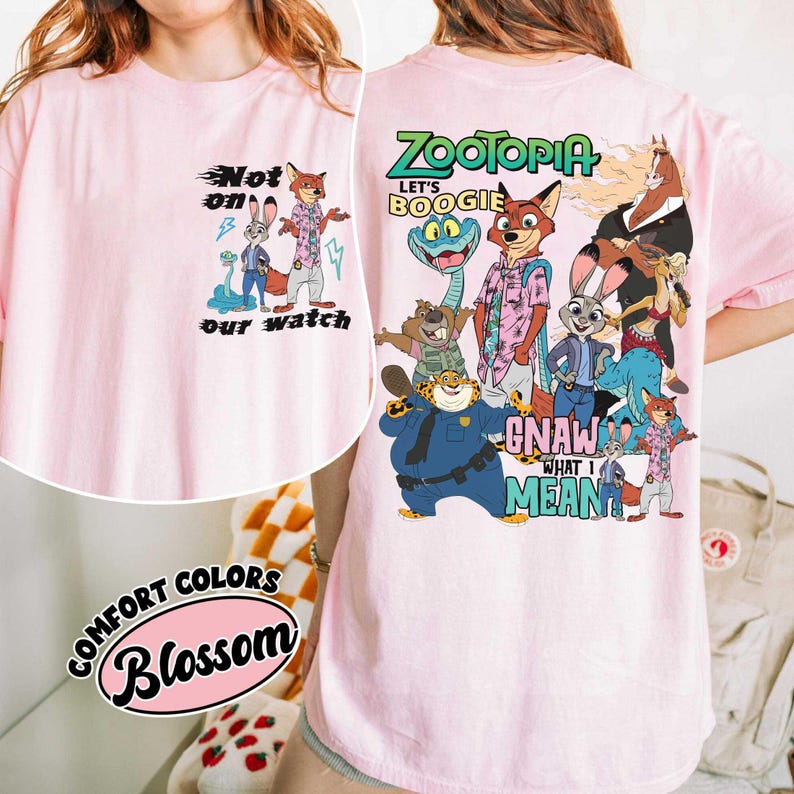May include: A light pink t-shirt featuring cartoon characters from Zootopia. The front of the shirt has the text "Not on our watch". The back of the shirt has the text "Zootopia Let's Boogie Gnaw What I Mean". The shirt is labeled "Comfort Colors Blossom".