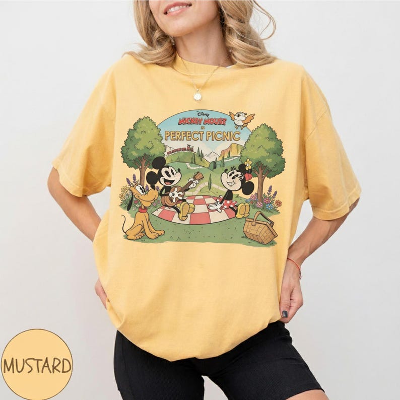 May include: Mustard yellow t-shirt featuring a vintage-style graphic of Mickey and Minnie Mouse having a picnic with Pluto. The graphic includes the text "Disney Mickey Mouse PERFECT PICNIC" in a retro font. The shirt is a casual, comfortable style.
