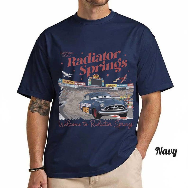 May include: Navy blue t-shirt featuring a graphic of a blue car racing on a track with the words "Radiator Springs" and "Welcome to Radiator Springs" in red. The shirt also has the text "California est. 2012".
