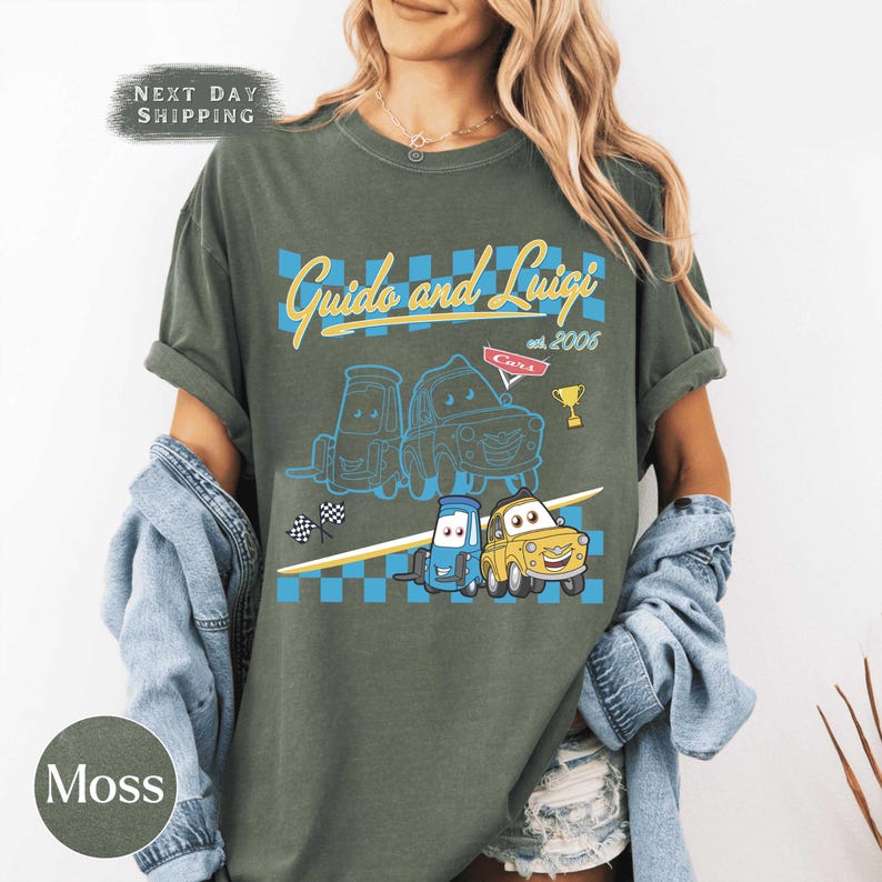 May include: Moss green t-shirt with the text "Guido and Luigi" and cartoon car illustrations. The design includes a checkered pattern, a trophy, and the text "Cars est. 2006".