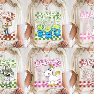 May include: Cream-colored t-shirts featuring various Toy Story characters like Woody, Aliens, Bo Peep, Buzz, Buttercup, and Jessie. Each design includes the character's name and the year 1995 within a checkered frame.