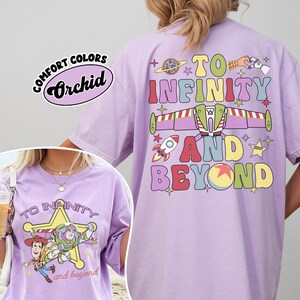 May include: A light purple t-shirt with the phrase "TO INFINITY AND BEYOND" in colorful letters and graphics. The shirt also features a graphic of Buzz Lightyear and Woody. The shirt has the words "Comfort Colors" and "Orchid" printed on it.
