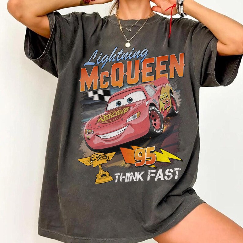 May include: Dark gray t-shirt featuring Lightning McQueen from the Cars movie. The graphic includes McQueen, the number 95, and the words "THINK FAST". The shirt has a vintage, distressed look.