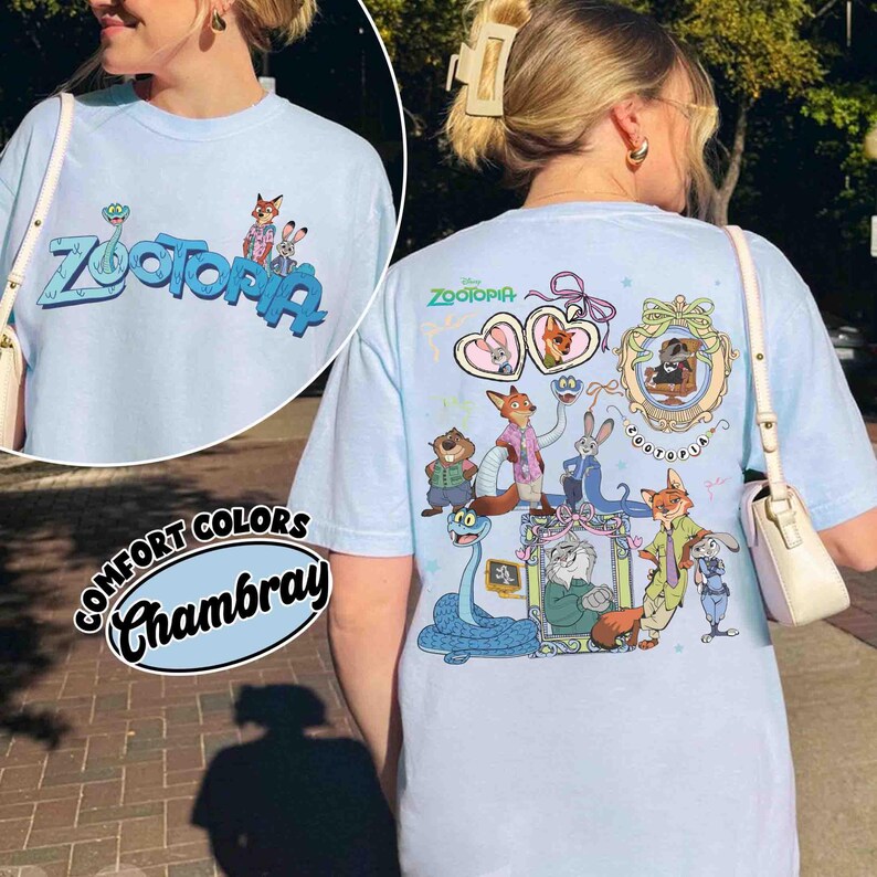 Puede incluir: Camiseta azul claro "Comfort Colors Chambray" con la palabra "Zootopia" y personajes de dibujos animados. La parte delantera muestra "Zootopia" en azul y verde. La parte trasera presenta varios personajes de dibujos animados.