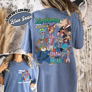 May include: Blue jean comfort colors t-shirt featuring characters from the movie Zootopia. The back of the shirt displays a colorful graphic with the text "Zootopia" and "Let's Boogie". The front of the shirt has a smaller graphic with the text "Not on our watch".