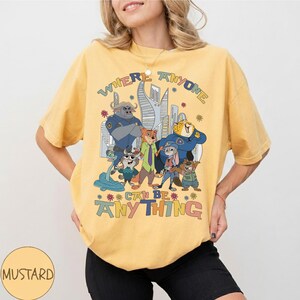 Puede incluir: Camiseta de color amarillo mostaza con un dise&ntilde;o gr&aacute;fico colorido de personajes de la pel&iacute;cula animada Zootopia. El dise&ntilde;o incluye el texto "WHERE ANYONE CAN BE ANYTHING". La camiseta es de estilo casual y c&oacute;modo.