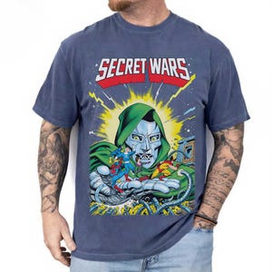May include: Blue t-shirt featuring the text "SECRET WARS" above a comic book illustration of Doctor Doom holding several superheroes. The graphic is in bright colors with a vintage comic book style.