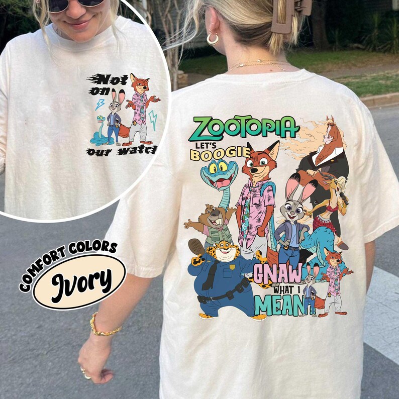 May include: Ivory-colored long-sleeve shirt featuring a graphic of characters from the animated film Zootopia. The front of the shirt has the text "Not on our watch". The back of the shirt has the text "Zootopia" and "Let's Boogie".