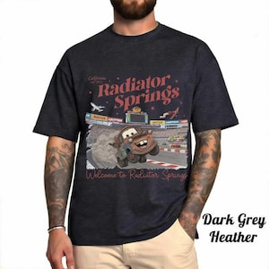 May include: Dark grey heather t-shirt featuring a graphic of Mater from the movie Cars racing on a track. The shirt has the text "Radiator Springs" and "Welcome to Radiator Springs" in red and white.