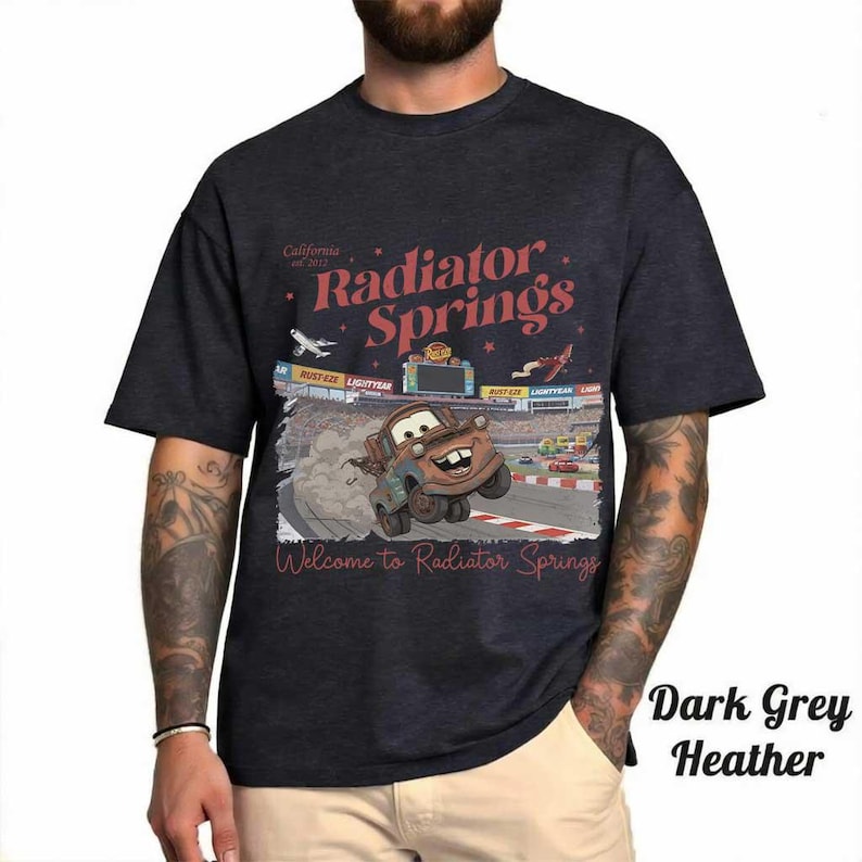 May include: Dark grey heather t-shirt featuring a graphic of Mater from the movie Cars racing on a track. The shirt has the text "Radiator Springs" and "Welcome to Radiator Springs" in red and white.