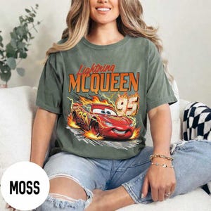 Puede incluir: Camiseta verde musgo con un dise&ntilde;o de Rayo McQueen de la pel&iacute;cula Cars. El dise&ntilde;o incluye el texto "Lightning McQueen" en naranja y un coche de carreras rojo con el n&uacute;mero "95" en llamas. La camiseta es de corte holgado.