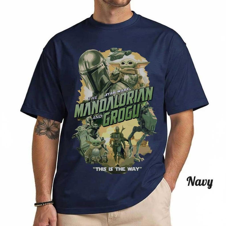 May include: A navy blue short-sleeve t-shirt featuring a graphic print of The Mandalorian and Grogu. The design includes the text "THE MANDALORIAN AND GROGU" and "THIS IS THE WAY" along with illustrations of characters and a walker vehicle.
