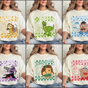 May include: Cream-colored t-shirts featuring cartoon characters from the movie Toy Story. Each shirt has a different character design with the character's name and the year 1995 in a colored checkered box. Characters include Slinky, Rex, Mr. Potato Head, Zurg, Mr. Pricklepants, and Mrs. Potato Head.