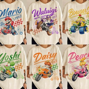 以下が含まれることがあります： 6枚のオフホワイトのTシャツのコレクション。それぞれ異なる任天堂のキャラクターがレース車両に乗っているデザインです。マリオ、ワルイージ、クッパJr.、ヨッシー、デイジー、ピーチが描かれており、1992という文字と市松模様が添えられています。