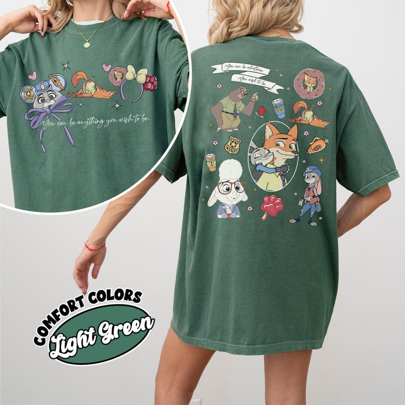 Puede incluir: Camiseta verde claro con ilustraciones de dibujos animados de Zootopia. La parte delantera presenta personajes y el texto "You can be anything you wish to be". La parte trasera tiene m&aacute;s personajes y el mismo texto. La camiseta est&aacute; etiquetada como "Comfort Colors".