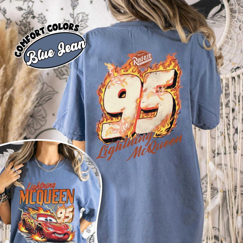 May include: Blue jean Comfort Colors t-shirt featuring a graphic of Lightning McQueen's number 95 in flames. The shirt also has the text "Lightning McQueen" and "Rust-eze".