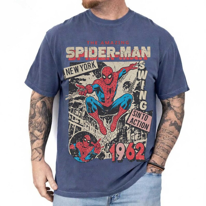 Pode incluir: Camiseta azul com um gr&aacute;fico vintage do Homem-Aranha. O design inclui as palavras "The Amazing Spider-Man", "New York" e "Swing Into Action", juntamente com o ano de "1962". O gr&aacute;fico mostra o Homem-Aranha em seu traje cl&aacute;ssico vermelho e azul.