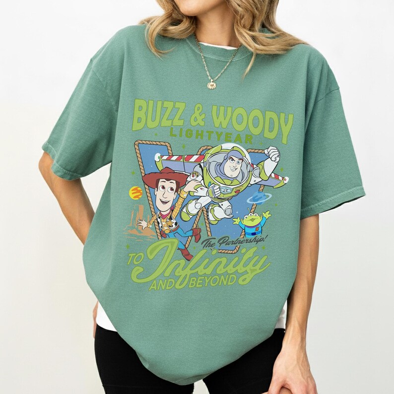 Peut inclure: Un t-shirt &agrave; manches courtes vert sauge avec une impression graphique de Buzz l'&Eacute;clair et Woody de Toy Story. Le texte indique BUZZ & WOODY LIGHTYEAR TO INFINITY AND BEYOND. Le motif inclut une bordure en corde, une petite plan&egrave;te et un extraterrestre.
