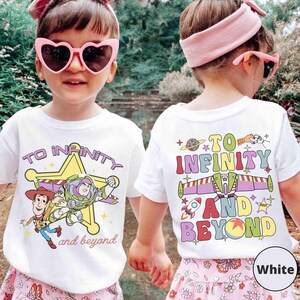 May include: White t-shirts with a colorful graphic featuring characters and text from the movie Toy Story. The front of the shirt says "TO INFINITY and beyond" with Woody and Buzz Lightyear. The back of the shirt says "TO INFINITY AND BEYOND".