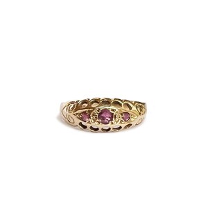 Peut inclure: Une bague en or dotée d'un anneau au motif alvéolé ajouré et de trois petites pierres précieuses rondes de couleur rose, serties horizontalement au centre. Le métal présente une finition polie et le design inclut des détails de volutes.