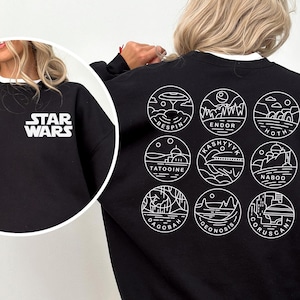 May include: Black sweatshirt with white "STAR WARS" text on the front and nine circular planet designs on the back. The designs include the names of planets like Bespin, Endor, and Tatooine. The sweatshirt has a white collar.