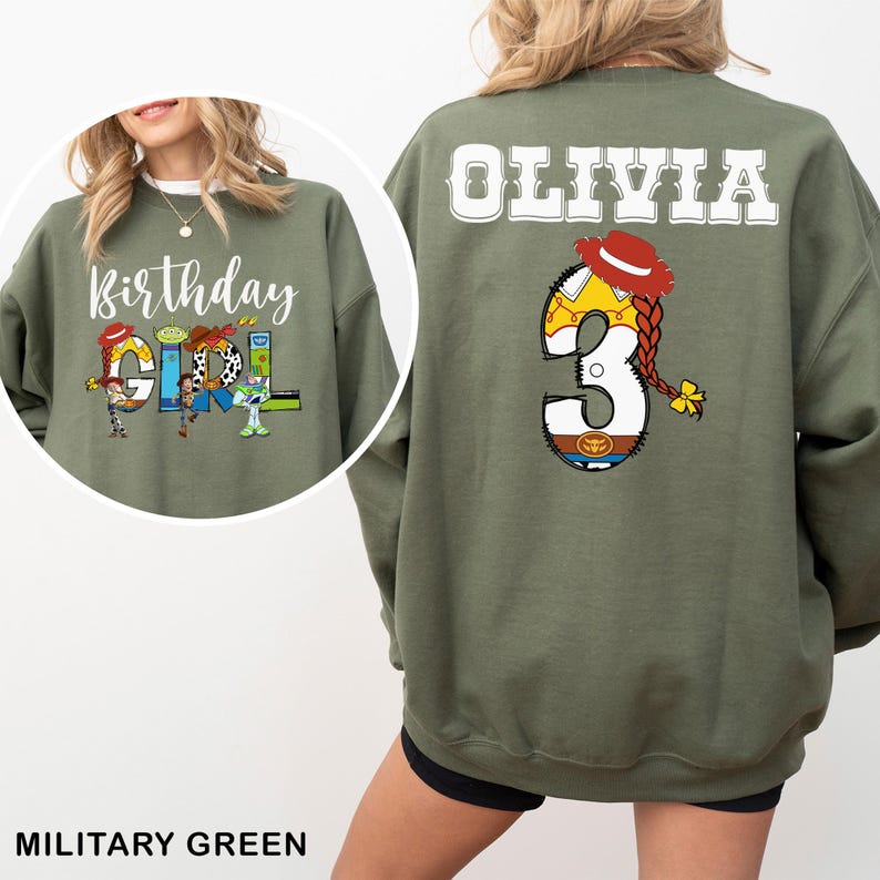 May include: Military green sweatshirt with the text "Birthday Girl" and Toy Story characters. The back features the name "Olivia" and the number "3" with a Toy Story theme. The sweatshirt is a comfortable, casual style.