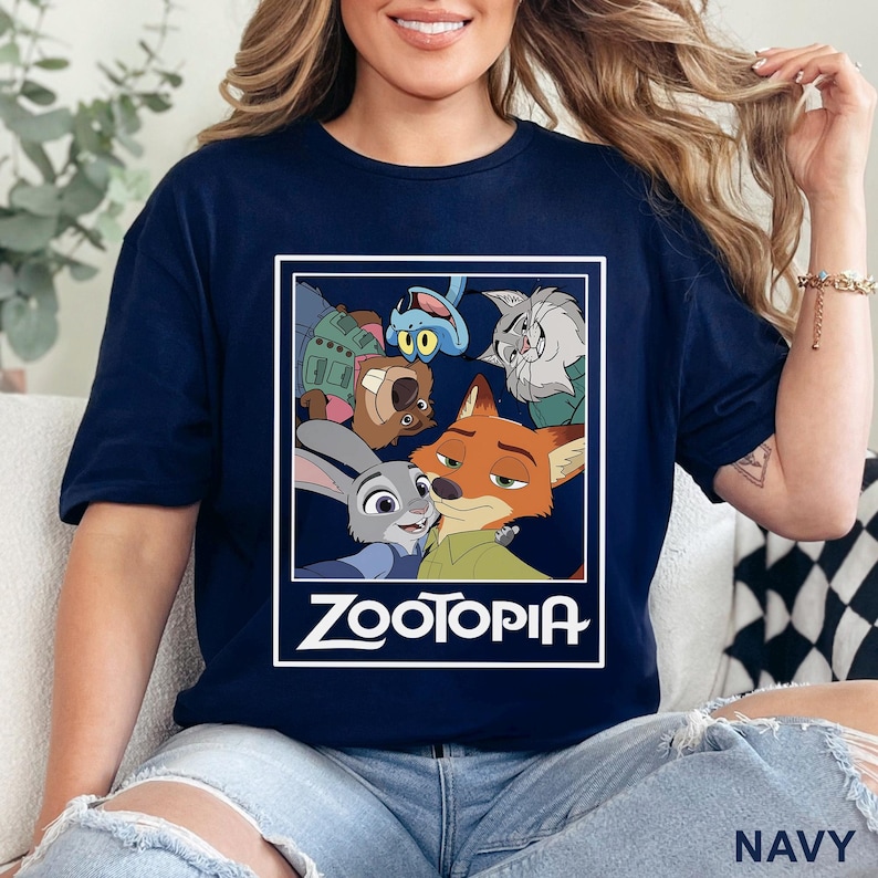 Peut inclure: T-shirt bleu marine avec un motif des personnages du film d'animation "Zootopie". Le motif comprend Judy Hopps, Nick Wilde et d'autres personnages dans un rectangle bord&eacute; de blanc. Le mot "ZOOTOPIA" est imprim&eacute; en blanc en dessous.