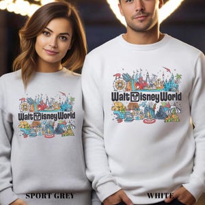Puede incluir: Sudaderas grises deportivas y blancas con un gr&aacute;fico colorido de Walt Disney World. El gr&aacute;fico incluye una noria, un castillo y otros iconos del parque. El texto "Walt Disney World" est&aacute; impreso debajo.