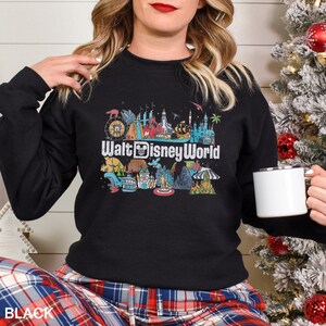 Puede incluir: Sudadera negra de cuello redondo con un gr&aacute;fico colorido de varios lugares emblem&aacute;ticos de Walt Disney World y el texto "Walt Disney World" en blanco. La sudadera es de color negro liso.