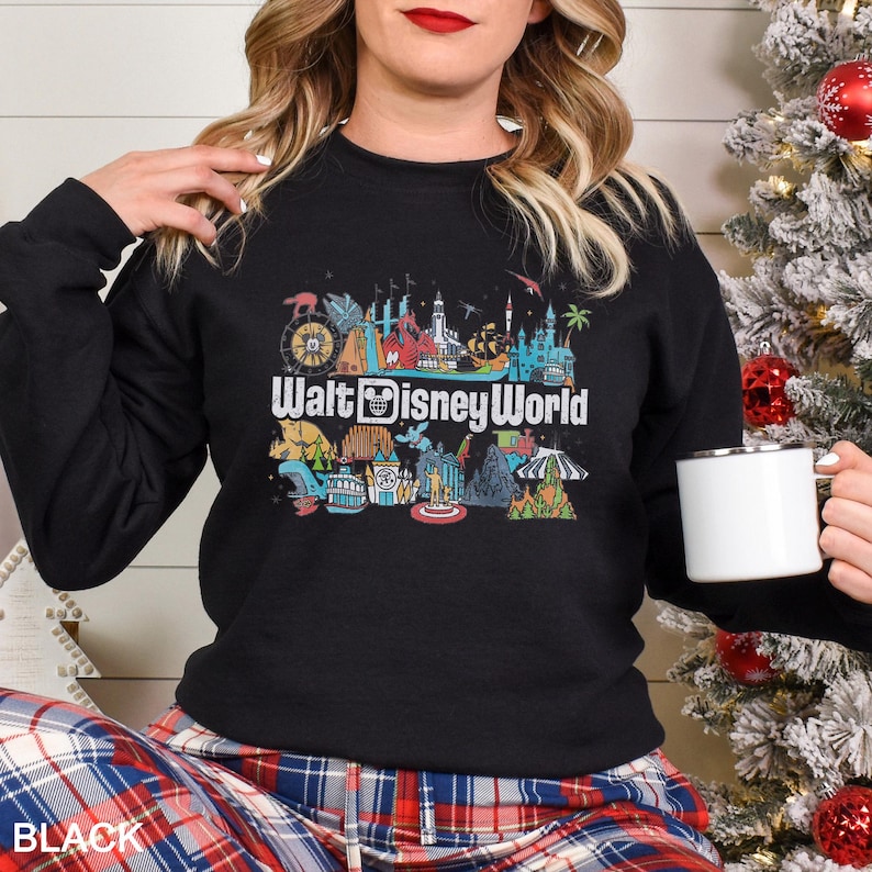 Puede incluir: Sudadera negra de cuello redondo con un gr&aacute;fico colorido de varios lugares emblem&aacute;ticos de Walt Disney World y el texto "Walt Disney World" en blanco. La sudadera es de color negro liso.