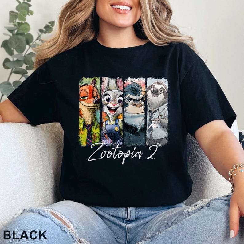 Peut inclure: T-shirt noir avec un graphisme color&eacute; des personnages de Zootopie 2. Le design comprend Nick Wilde, Judy Hopps, le chef Bogo et Flash. Les mots "Zootopia 2" sont &eacute;crits en cursive en dessous des personnages. Le mot "BLACK" est en bas.