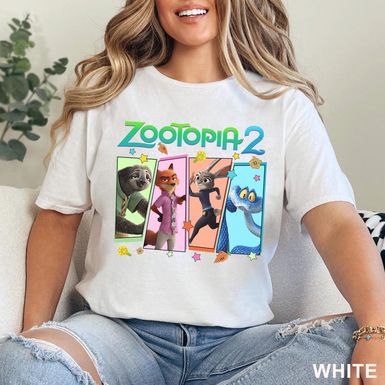 May include: White t-shirt with the text "ZOOTOPIA 2" in green and a colourful graphic of characters from the animated film. The graphic includes a sloth, fox, rabbit, and snake. The word "WHITE" is printed at the bottom.