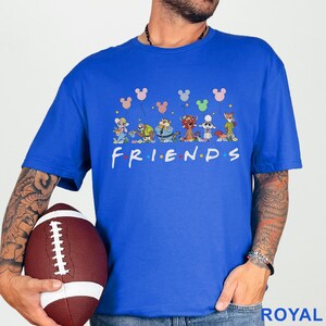 May include: Royal blue t-shirt with a cartoon design featuring characters and Mickey Mouse-shaped balloons. The word "FRIENDS" is printed in white. The shirt is a crew neck style.