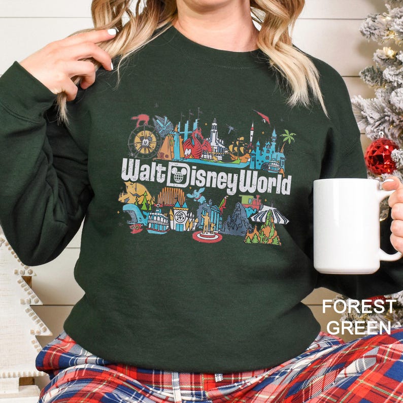 Puede incluir: Sudadera verde bosque con un gr&aacute;fico colorido de los monumentos de Walt Disney World y el texto "Walt Disney World" en blanco. La sudadera es de manga larga y cuello redondo.