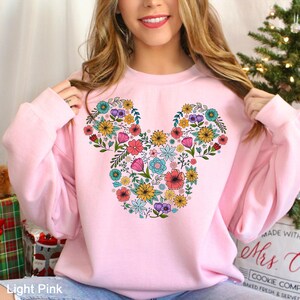 Puede incluir: Sudadera rosa claro con un dise&ntilde;o floral de Mickey Mouse. El dise&ntilde;o est&aacute; compuesto por varias flores coloridas, incluyendo rosas, amarillas, azules y moradas. La sudadera es de estilo cuello redondo.