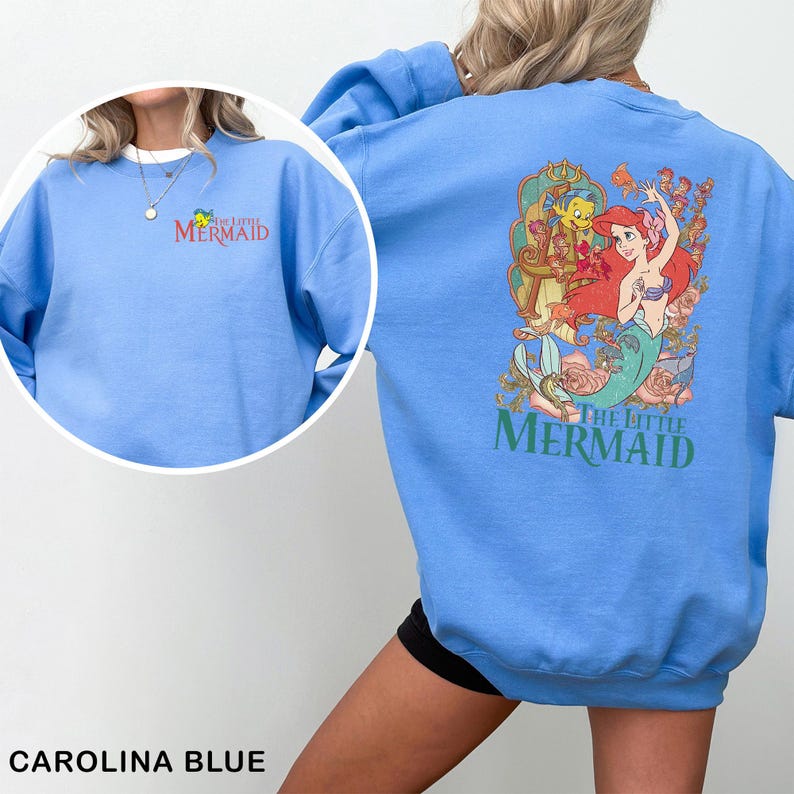 Op de afbeelding: Carolina blauwe sweatshirt met de tekst "The Little Mermaid" in groen en rood. De voorkant heeft een klein logo en de achterkant toont een kleurrijke afbeelding van Ariel, Botje en Sebastiaan. Een casual, comfortabele top.