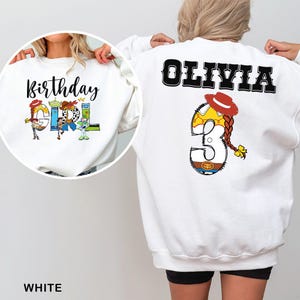 May include: White sweatshirt featuring the text "Birthday Girl" with colorful Toy Story character graphics. The back of the sweatshirt displays the name "Olivia" and a large number "3" with a Jessie-inspired design, including a red hat and braid.