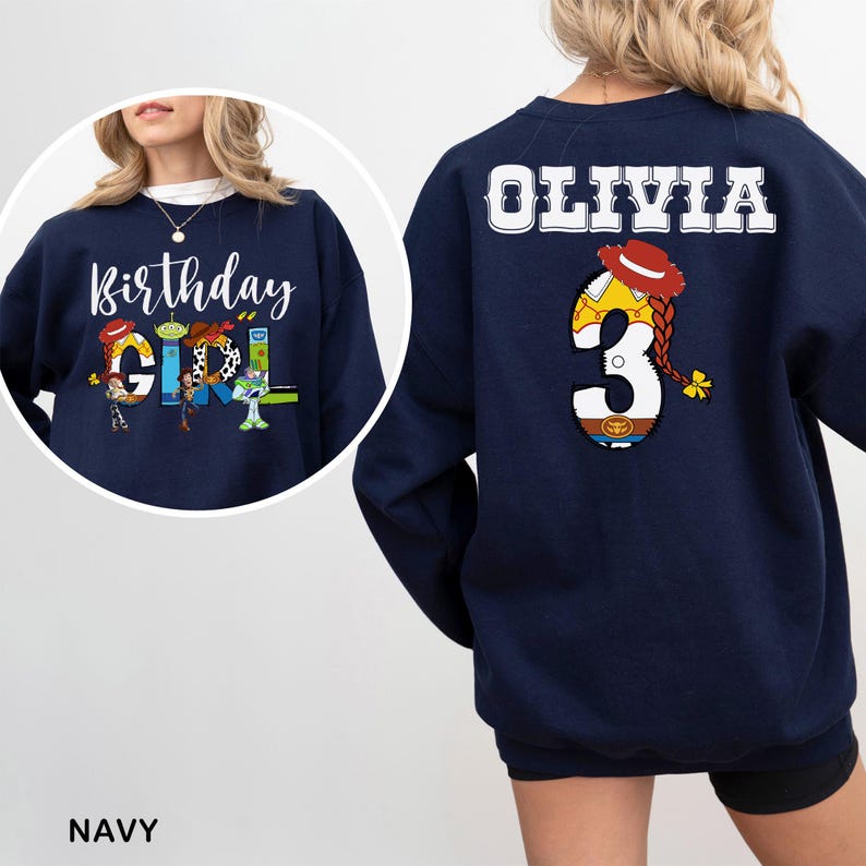 May include: Navy blue sweatshirt with "Birthday Girl" and character graphics on the front. The back features the name "Olivia" and a number "3" with a cowgirl design. The sweatshirt is a comfortable, casual style.