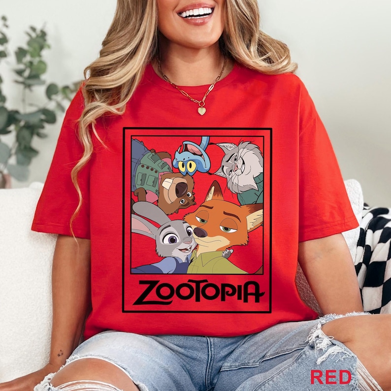Peut inclure: T-shirt rouge avec un motif du film d'animation Zootopie. Le motif comprend des personnages comme Judy Hopps et Nick Wilde, avec le mot "ZOOTOPIA" en noir. Le t-shirt est de couleur rouge vif.