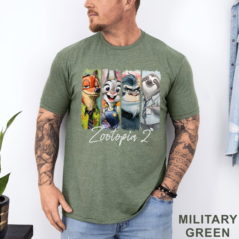 Peut inclure: T-shirt vert militaire avec un graphisme color&eacute; des personnages de Zootopia 2 : un renard, un lapin, un rhinoc&eacute;ros et un paresseux. Le texte "Zootopia 2" est &eacute;crit en blanc en dessous des personnages.