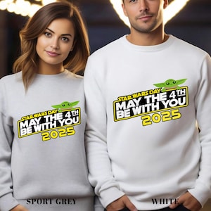 May include: Sport grey and white sweatshirts with a Star Wars Day graphic. The graphic includes the text "May the 4th Be With You 2025" with a green Yoda character. The bottom of the sweatshirts have the color names.