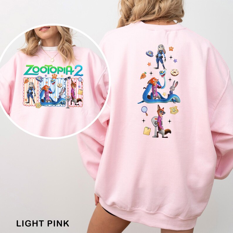 May include: Light pink sweatshirt featuring the text "ZOOTOPIA 2" on the front, with cartoon characters. The back of the sweatshirt has a colorful graphic of characters and objects from the movie. The sweatshirt is made of a soft material.
