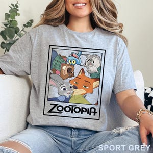 Peut inclure: T-shirt gris sport avec un motif du film d'animation Zootopie. Le motif comprend des personnages comme Judy Hopps et Nick Wilde, avec le titre du film en dessous. Le t-shirt est de couleur gris clair.