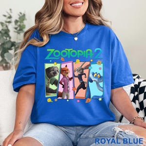 May include: Royal blue t-shirt with the text "Zootopia 2" and a rectangular graphic featuring four cartoon characters: a sloth, fox, rabbit, and snake. The shirt is a solid royal blue colour.