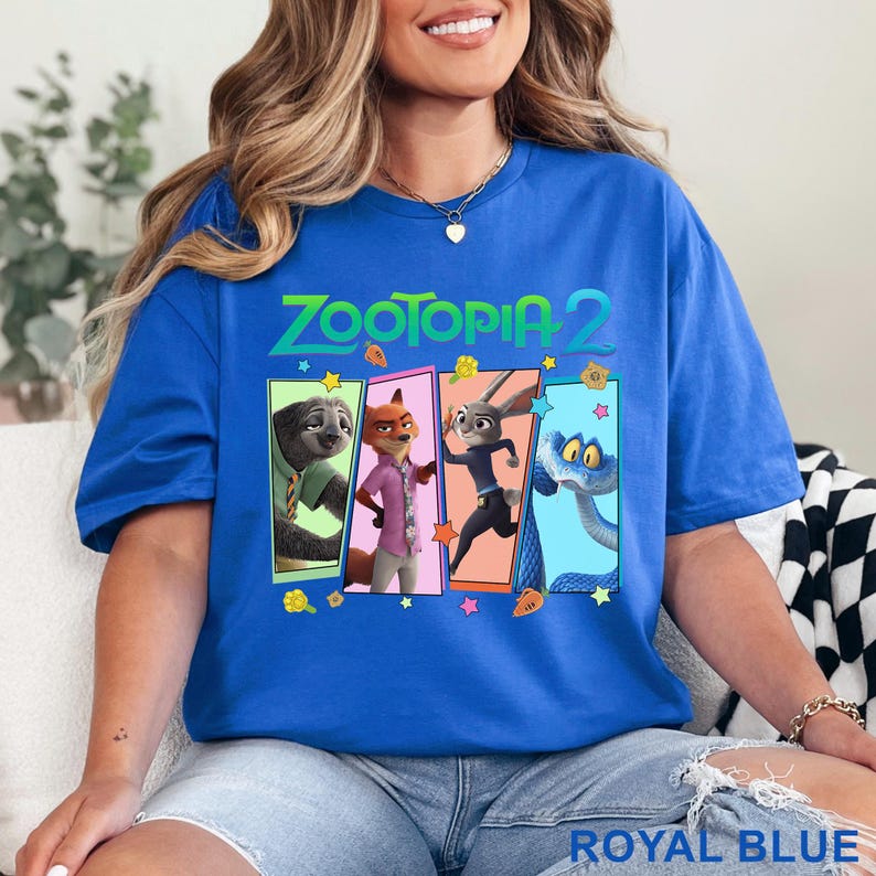 May include: Royal blue t-shirt with the text "Zootopia 2" and a rectangular graphic featuring four cartoon characters: a sloth, fox, rabbit, and snake. The shirt is a solid royal blue colour.