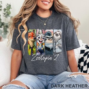 Peut inclure: T-shirt gris fonc&eacute; avec des personnages de Zootopie. Le graphisme comprend Nick Wilde, Judy Hopps, un gorille et Flash le paresseux. Le texte "Zootopia 2" est &eacute;crit en blanc. Le bas du t-shirt indique "DARK HEATHER".