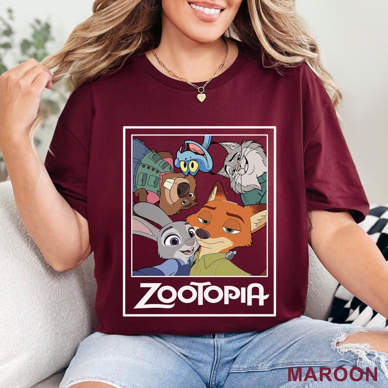 Peut inclure: T-shirt bordeaux avec un graphisme des personnages du film d'animation Zootopie. Le design comprend Judy Hopps, Nick Wilde et d'autres personnages dans un cadre rectangulaire blanc. Le mot "ZOOTOPIA" est imprim&eacute; en blanc.
