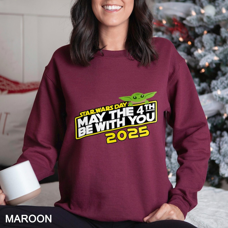 May include: Maroon sweatshirt with a Star Wars Day graphic featuring Yoda and the text "May the 4th Be With You 2025". The design is in yellow and green. The word "MAROON" is printed at the bottom of the image.