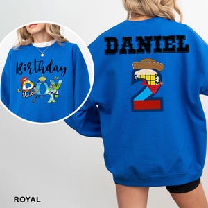 May include: Royal blue sweatshirt with the text "Birthday Boy" and a graphic of a cartoon character on the front. The back of the sweatshirt has the name "DANIEL" and a number 2 with a cowboy hat and bandana design.